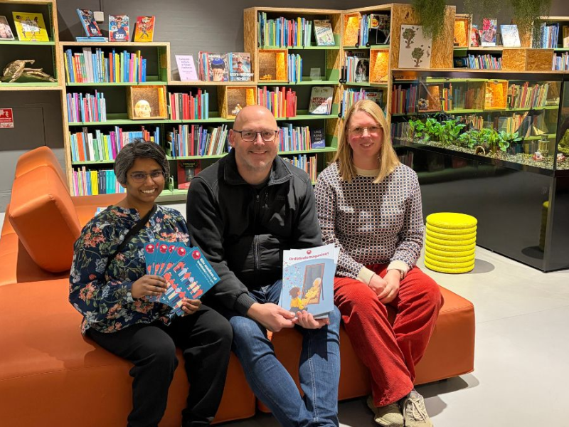 Billede af de tre mennesker, der afholder Ordblindecaféen. De sidder i en orange sofa i Outdoorbiblioteket, Silkeborg Bibliotek. 